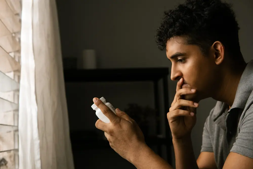 A man looks at his phone beside a window.