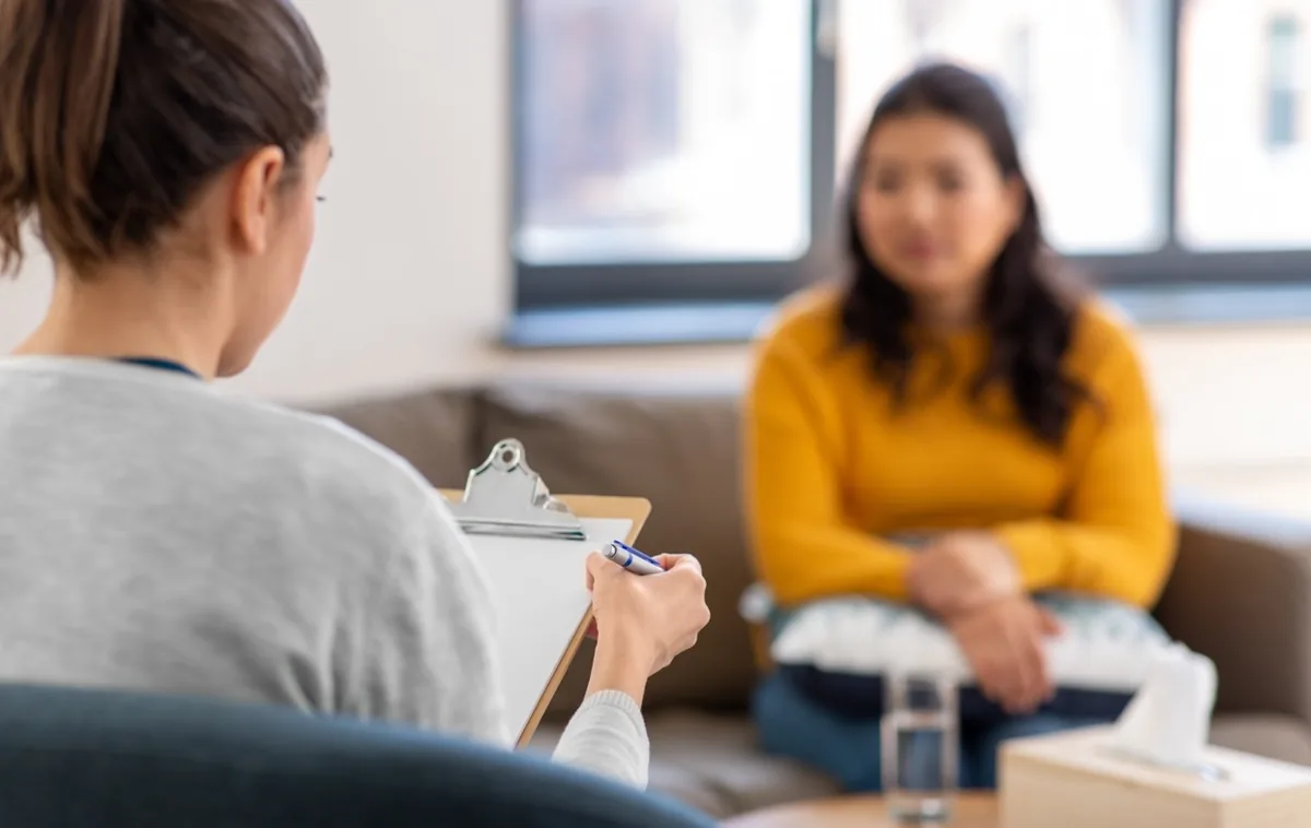 A counselor listens to a woman seated in a bright room.