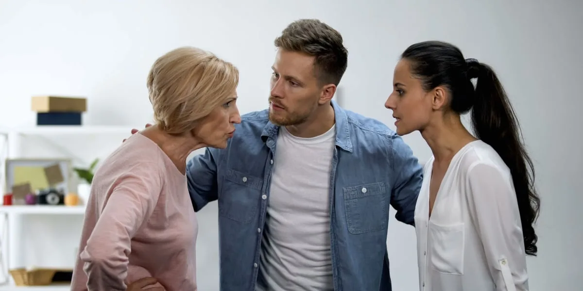 Two adults and an older woman talk together indoors.