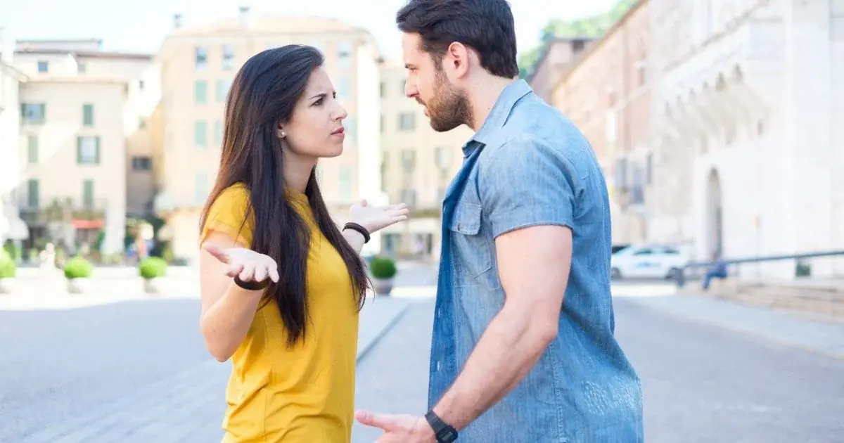 Two adults talk face to face on a city sidewalk.