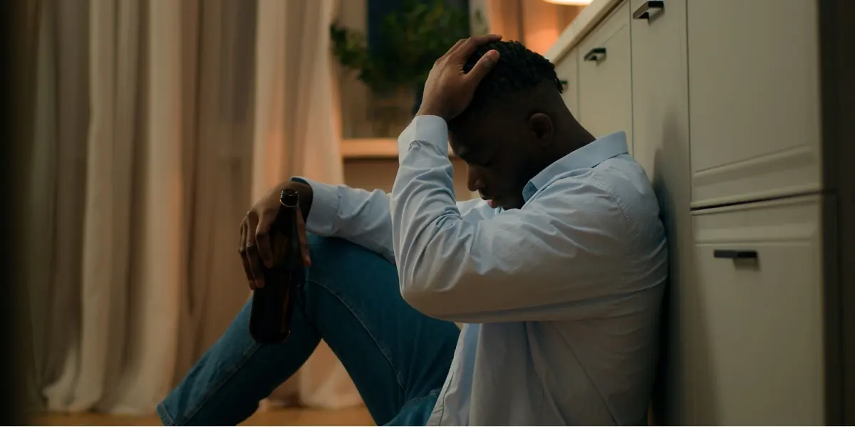 A man sits quietly on the floor beside a curtain.