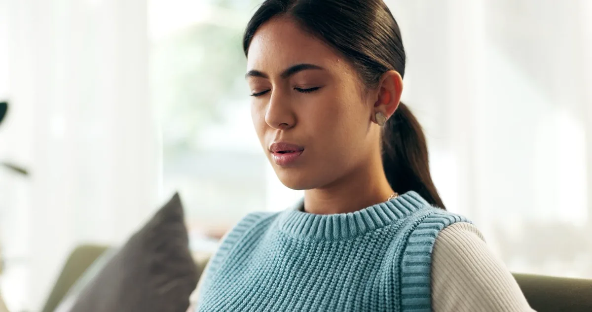 A woman sits quietly with her eyes closed, focusing on her breathing.
