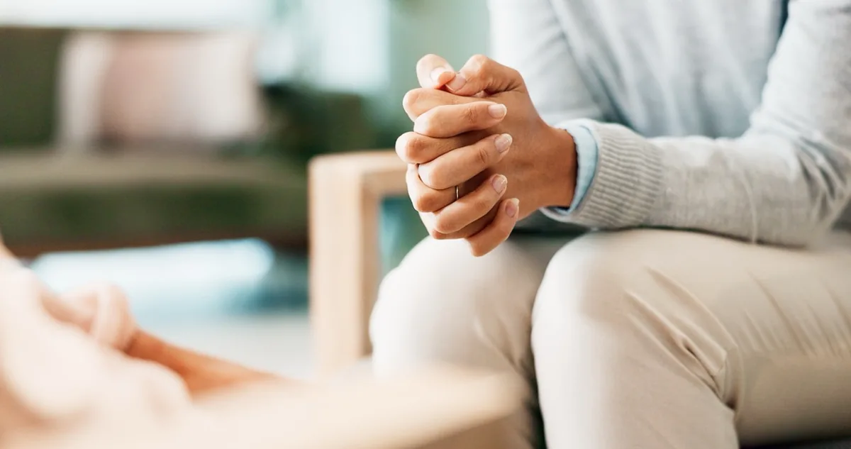 An adult sits with hands clasped during a conversation.