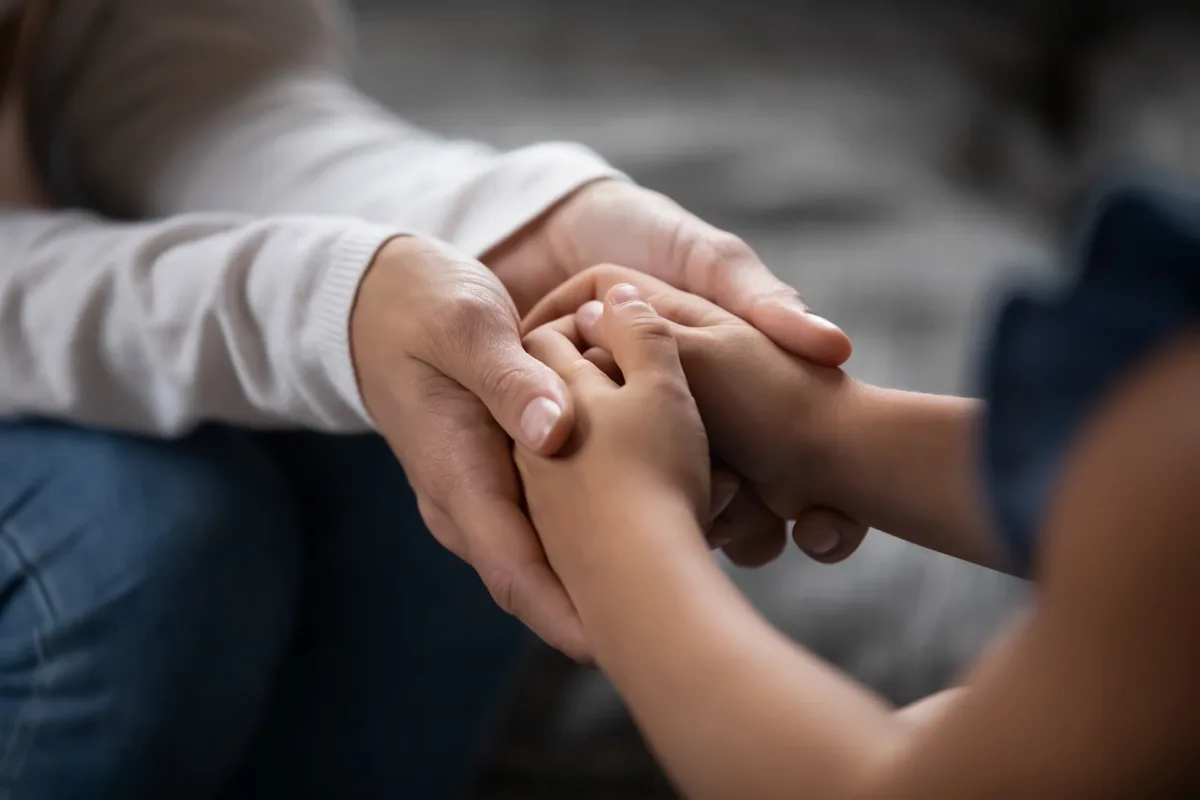 One person gently holds another person's hands.