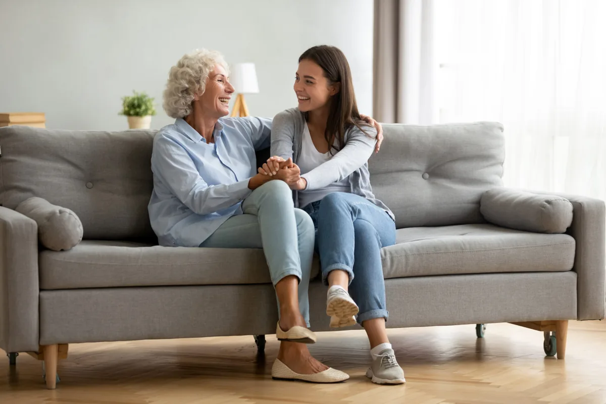 An older woman and a younger woman talk together on a sofa.