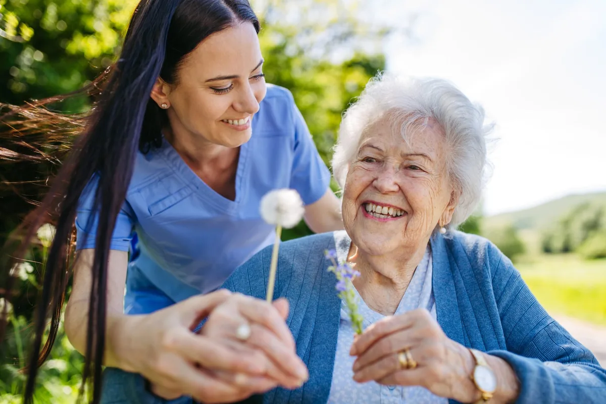 A caregiver and older woman smile together in a garden.