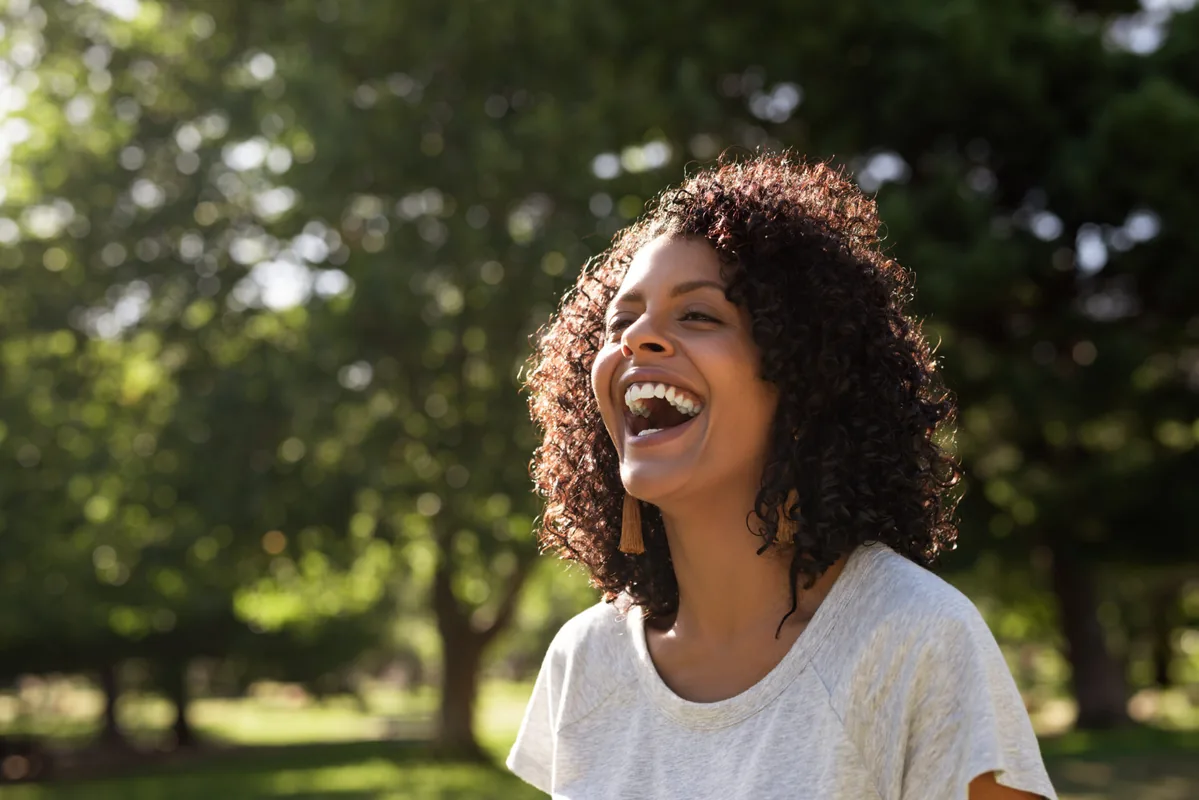 A woman laughs beneath the green leaves of a tree.