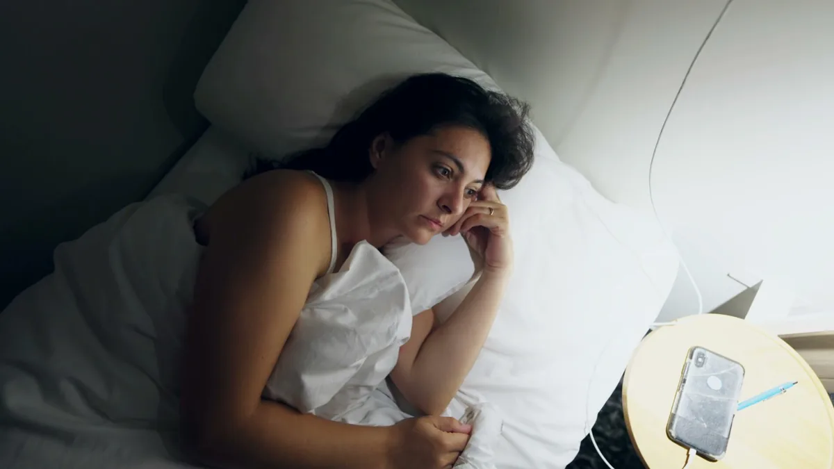 A woman lies awake at night beside an alarm clock.