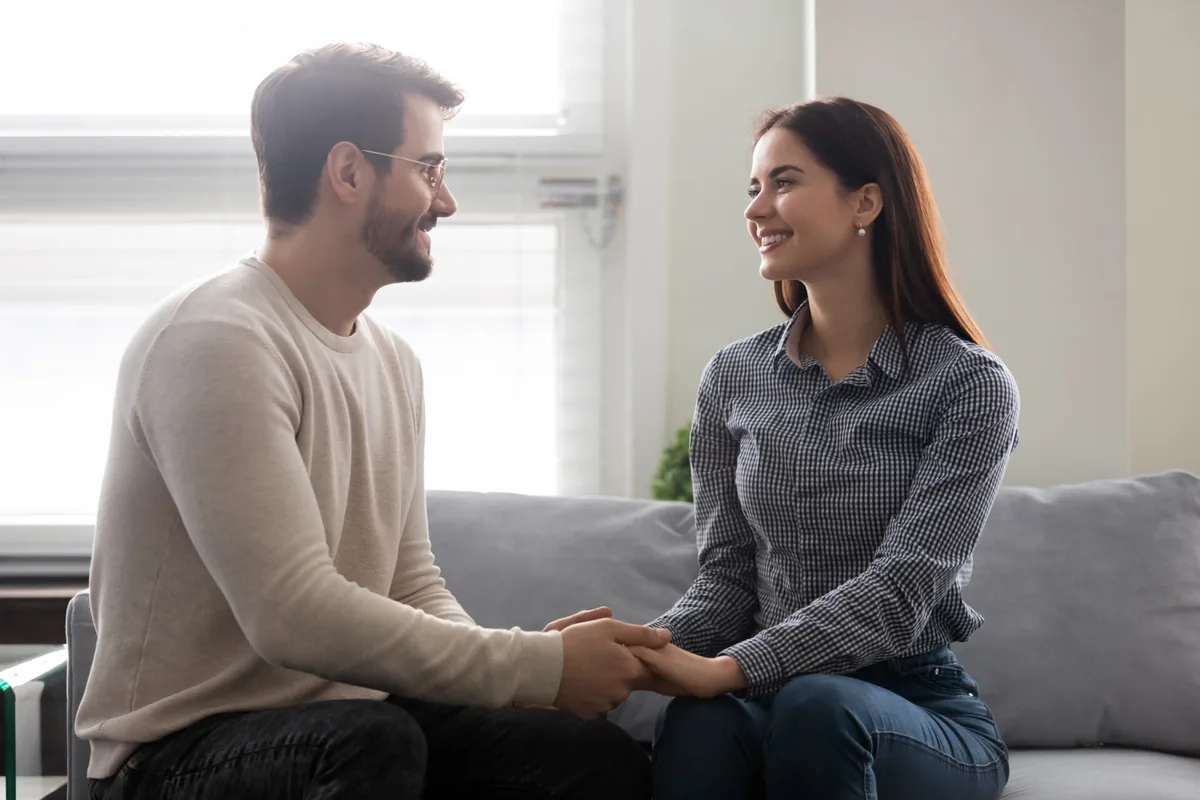 A couple sits together and holds hands while talking.