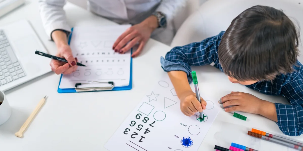 A child writes on paper while an adult helps with a learning activity.