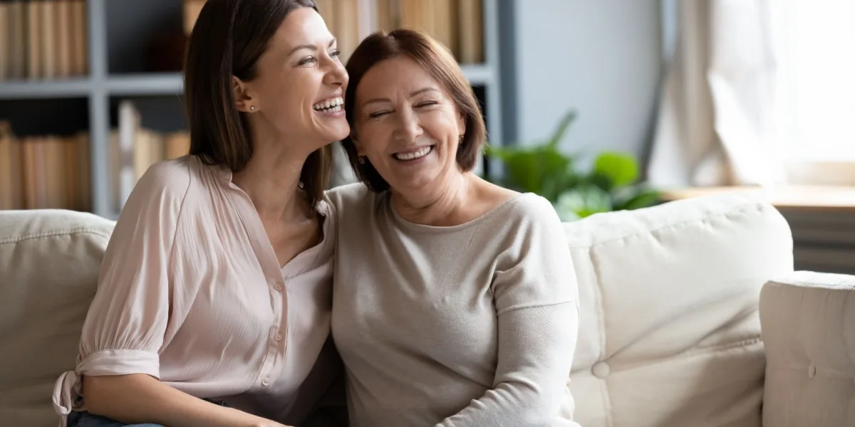 Two women share a laugh while sitting together on a sofa.