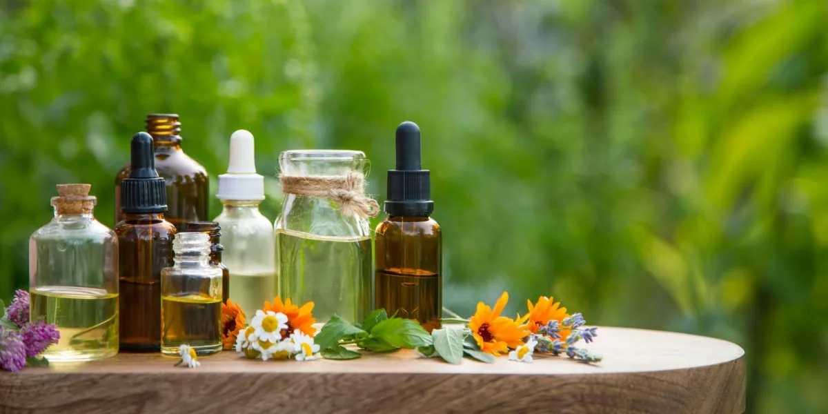 Small bottles and flowering plants sit on a wooden table in a garden.