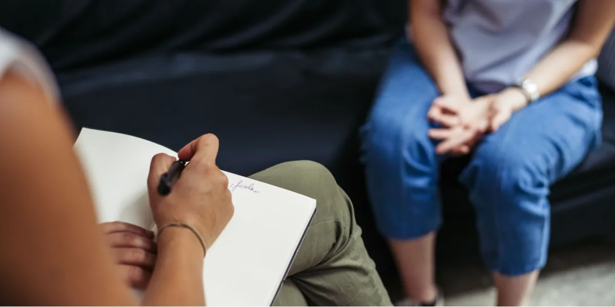 A counselor takes notes during a conversation with an adult.