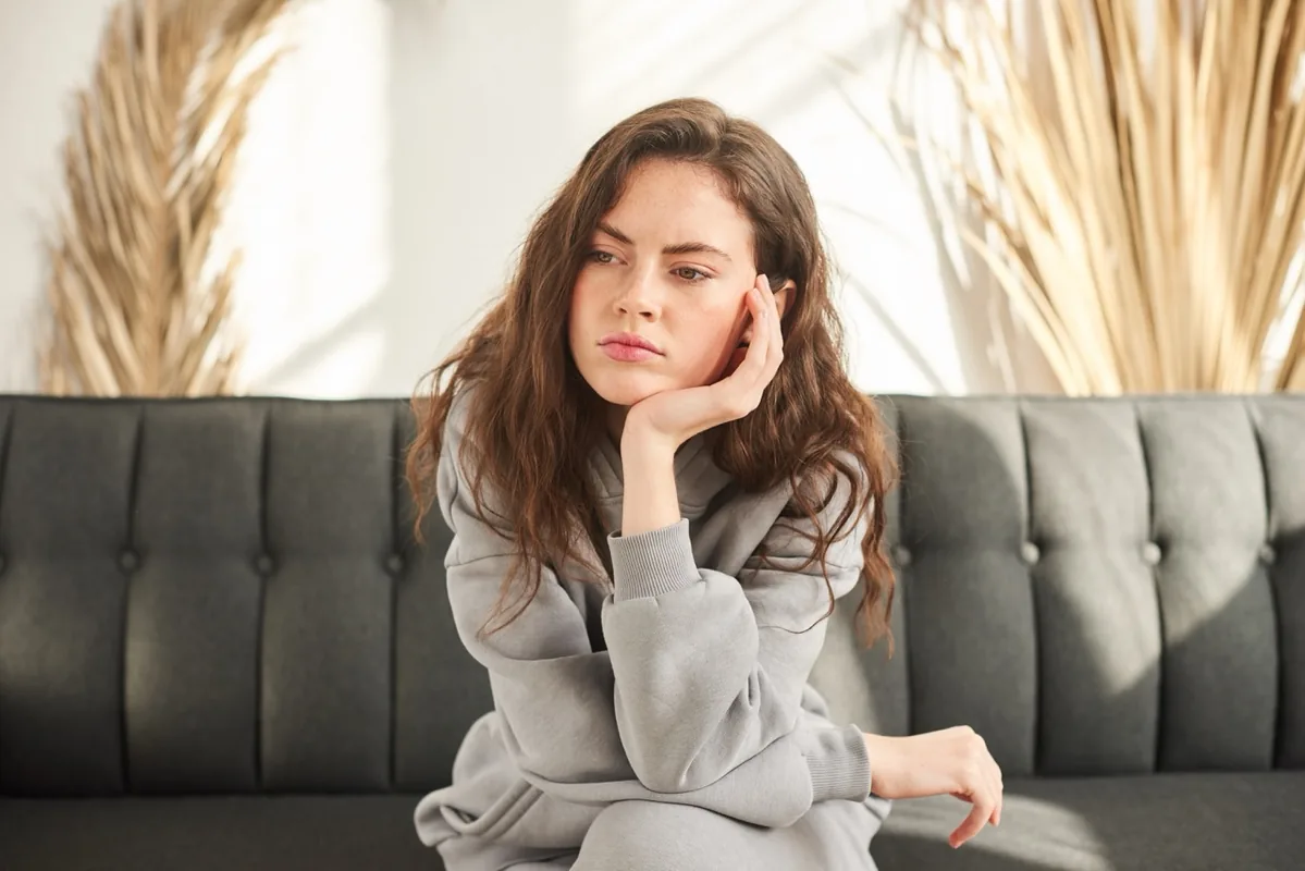 A woman rests her chin on one hand while seated indoors.