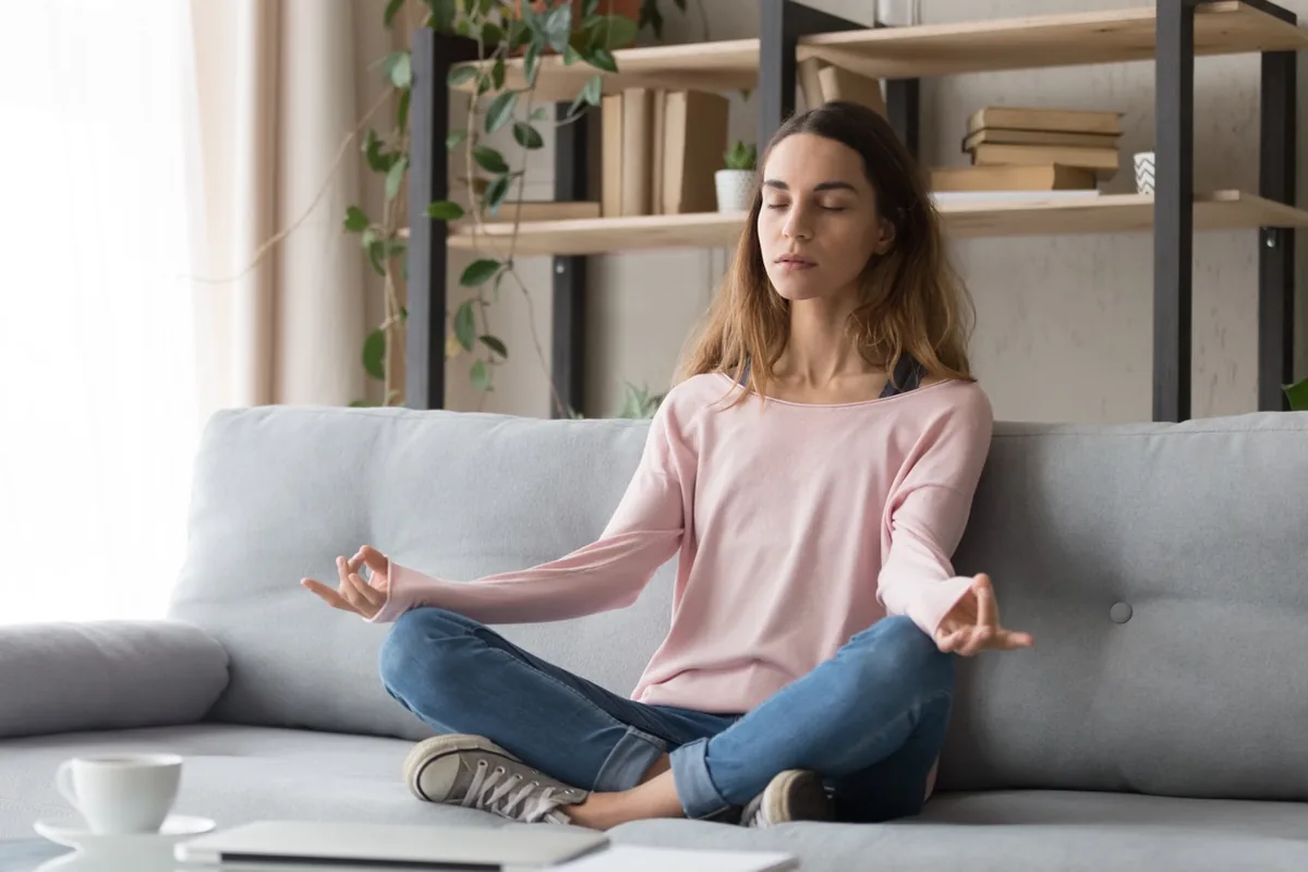 A woman practices seated meditation on a sofa.