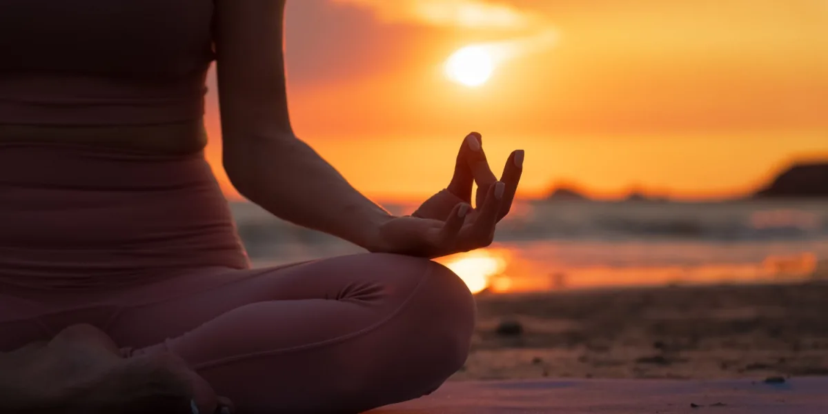 A person sits in meditation beside the sea at sunset.