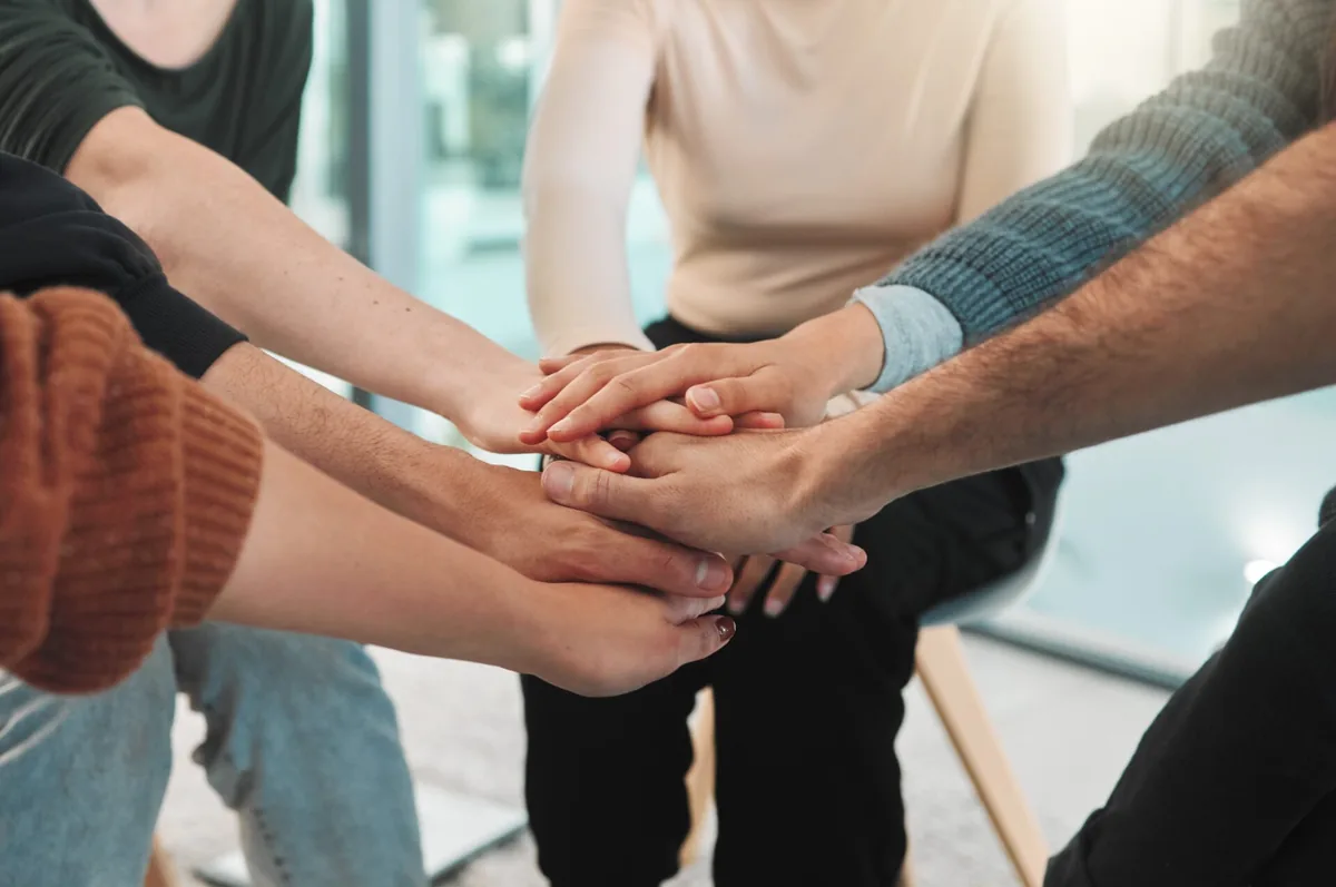 People place their hands together in a supportive group gesture.