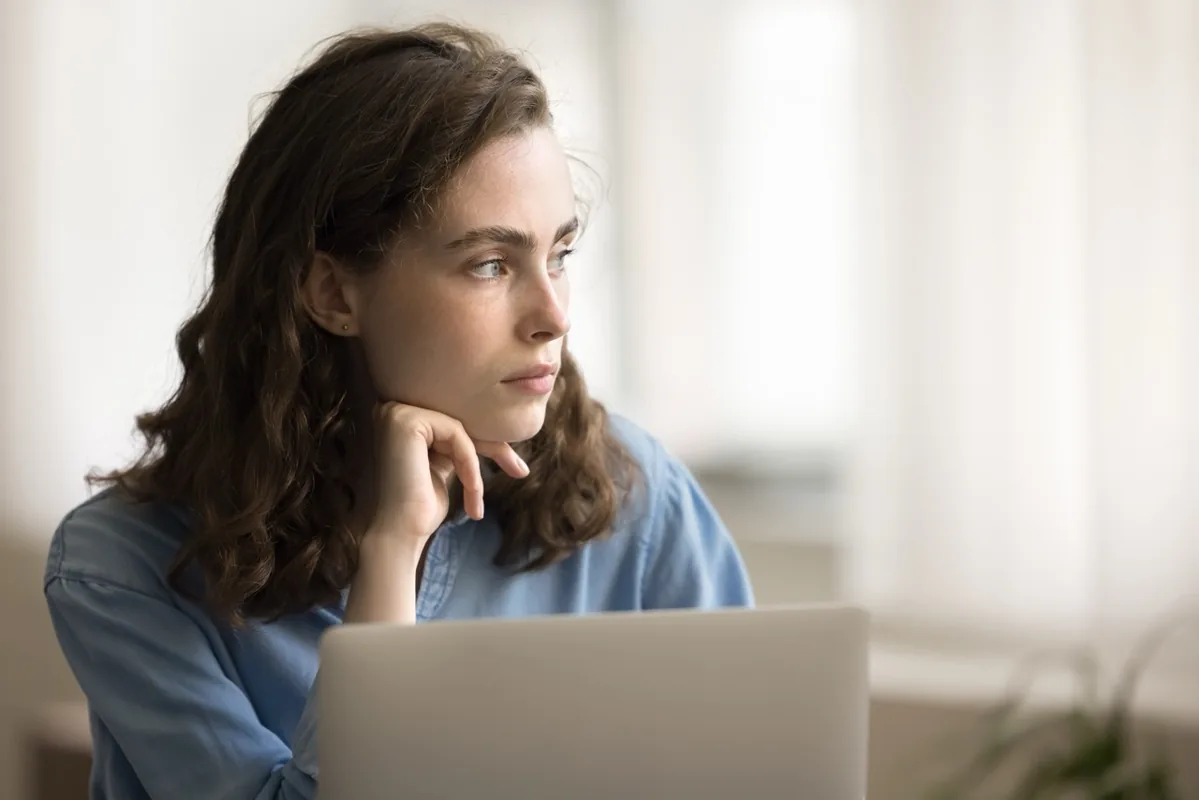 A woman takes a thoughtful break while working on a laptop.
