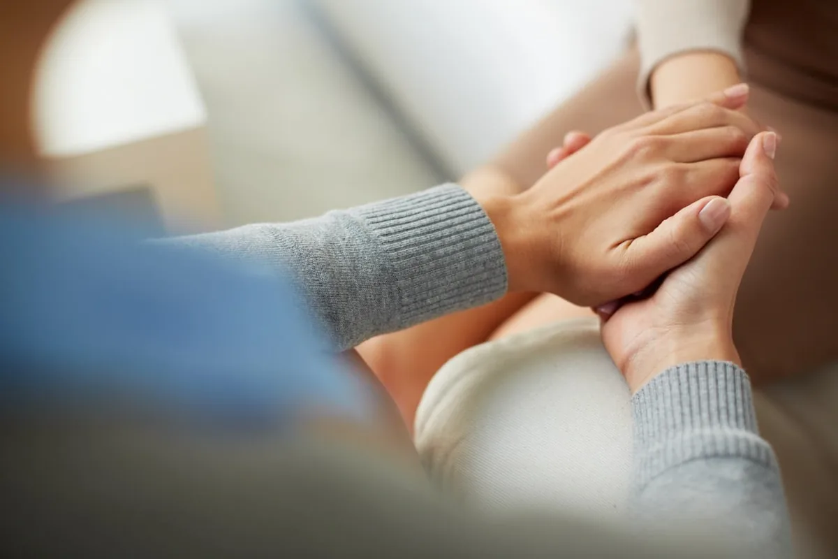A person rests a reassuring hand on another person's arm.
