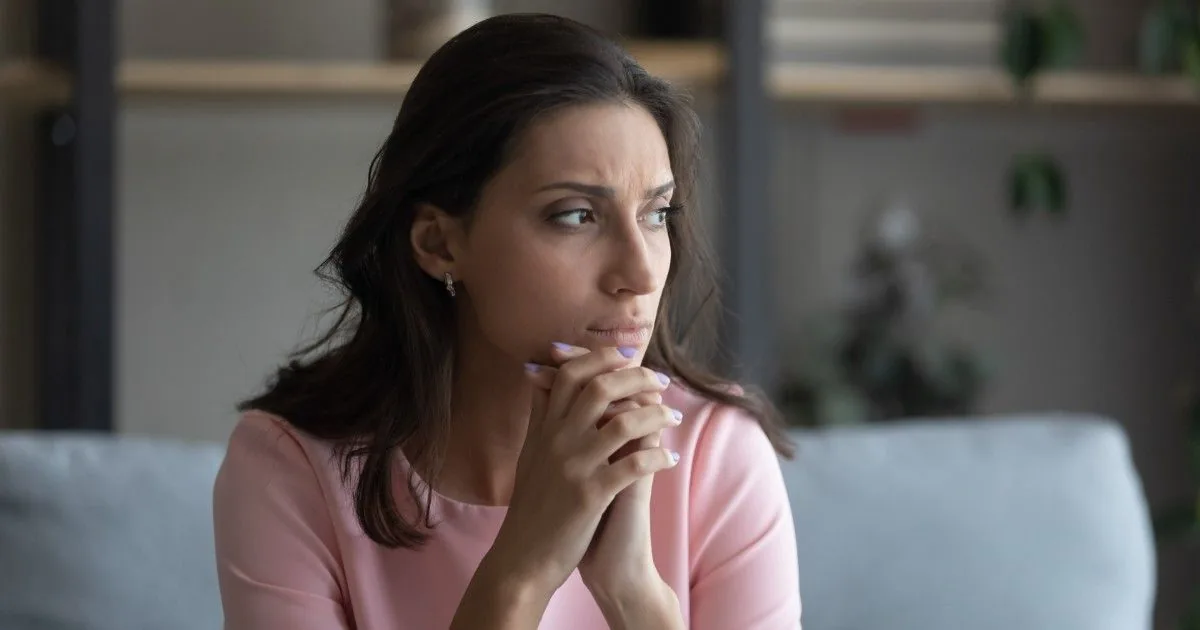 A woman pauses thoughtfully with her hands near her chin.
