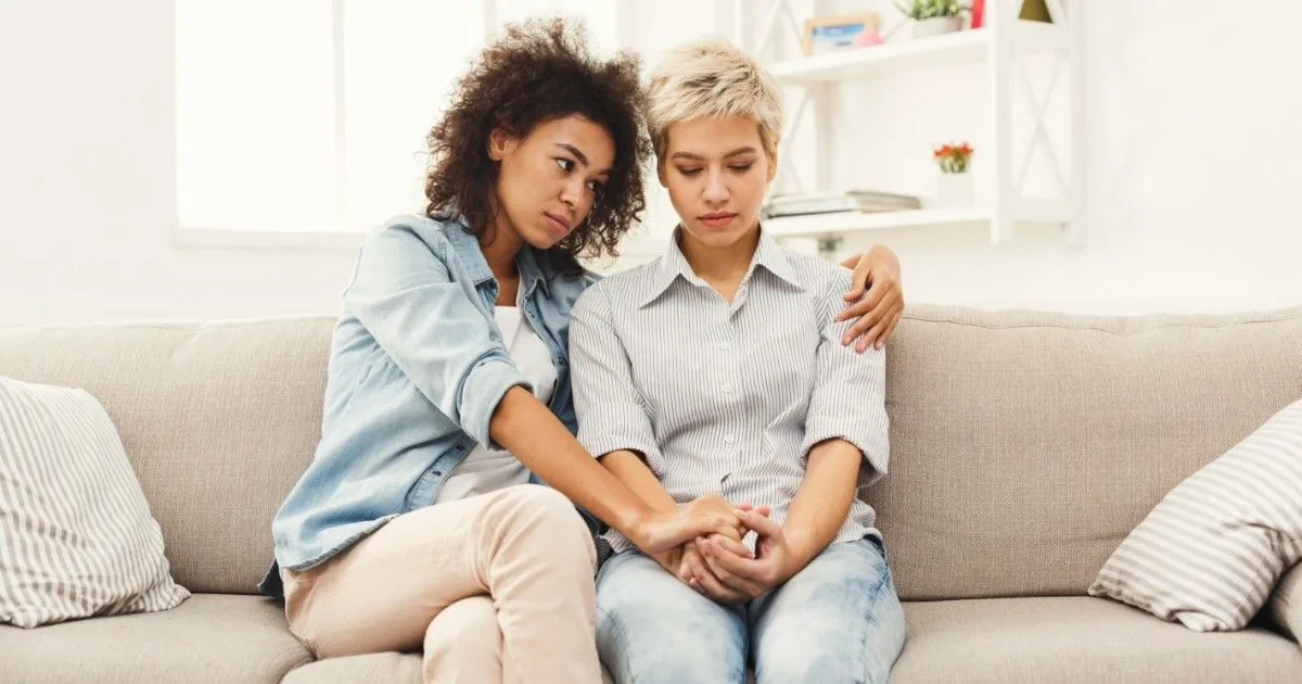Two friends sit close together and talk on a sofa.