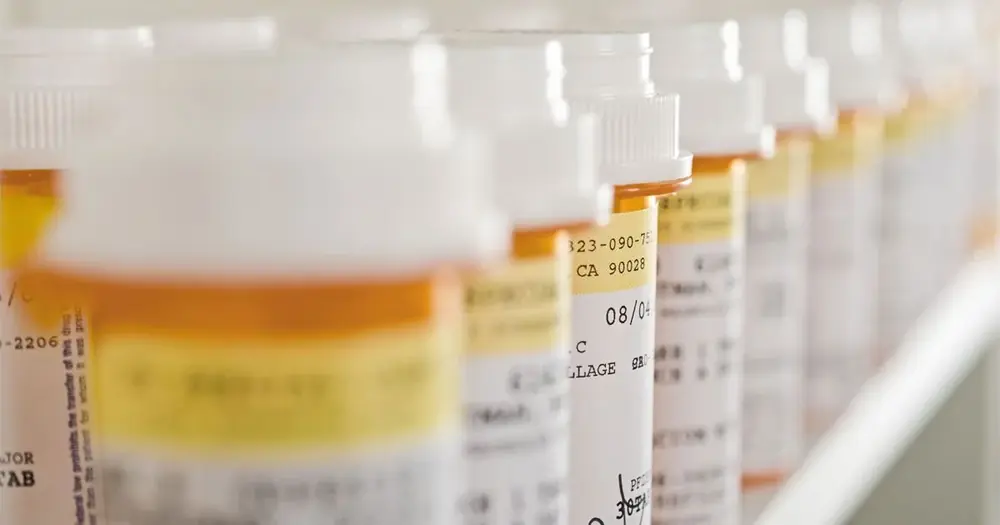 Prescription medicine bottles line a pharmacy shelf.