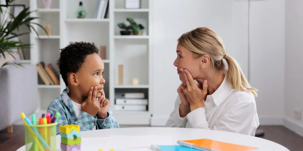 A healthcare professional speaks with a child at a table.