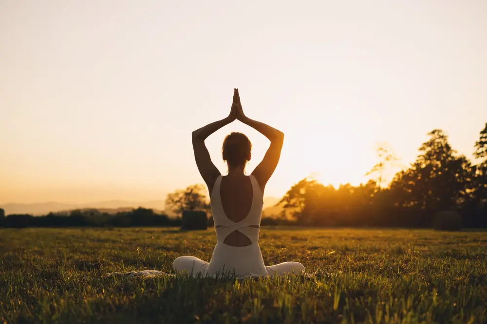 A person stretches into a yoga pose outdoors at sunset.