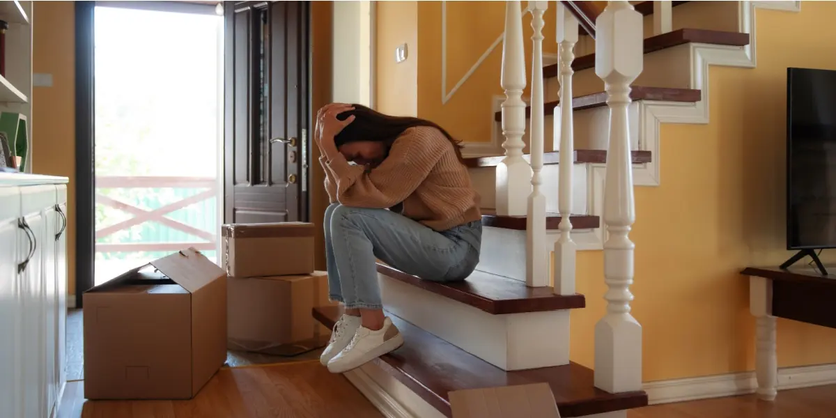 A woman sits beside moving boxes on a staircase.