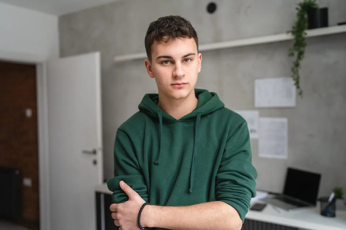 A young adult sits at a desk in a bright room.