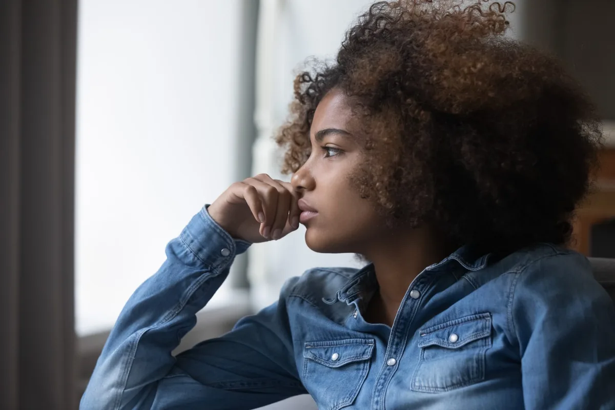 A woman sits on a sofa and looks thoughtfully to one side.