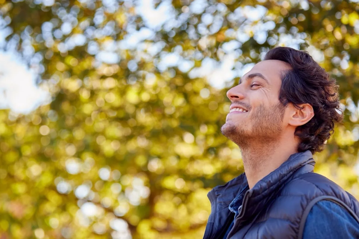 A man closes his eyes and enjoys the sunlight beneath a tree.
