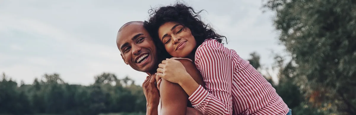 A couple embraces outdoors beneath a cloudy sky.