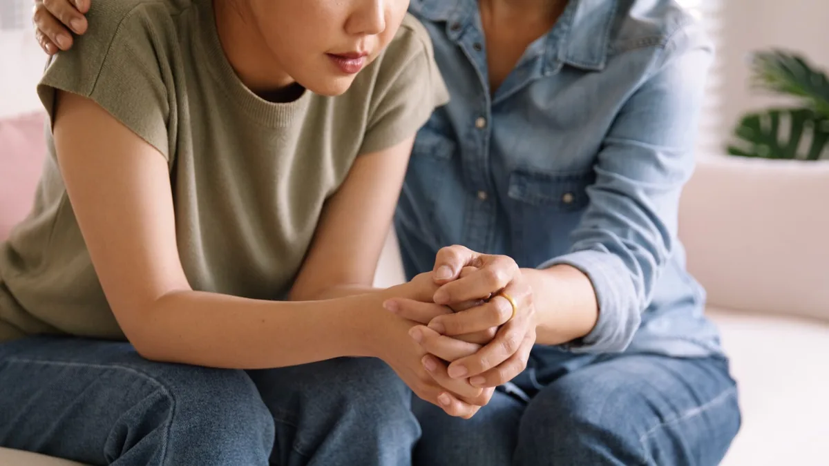 One person gently holds another person's clasped hands.