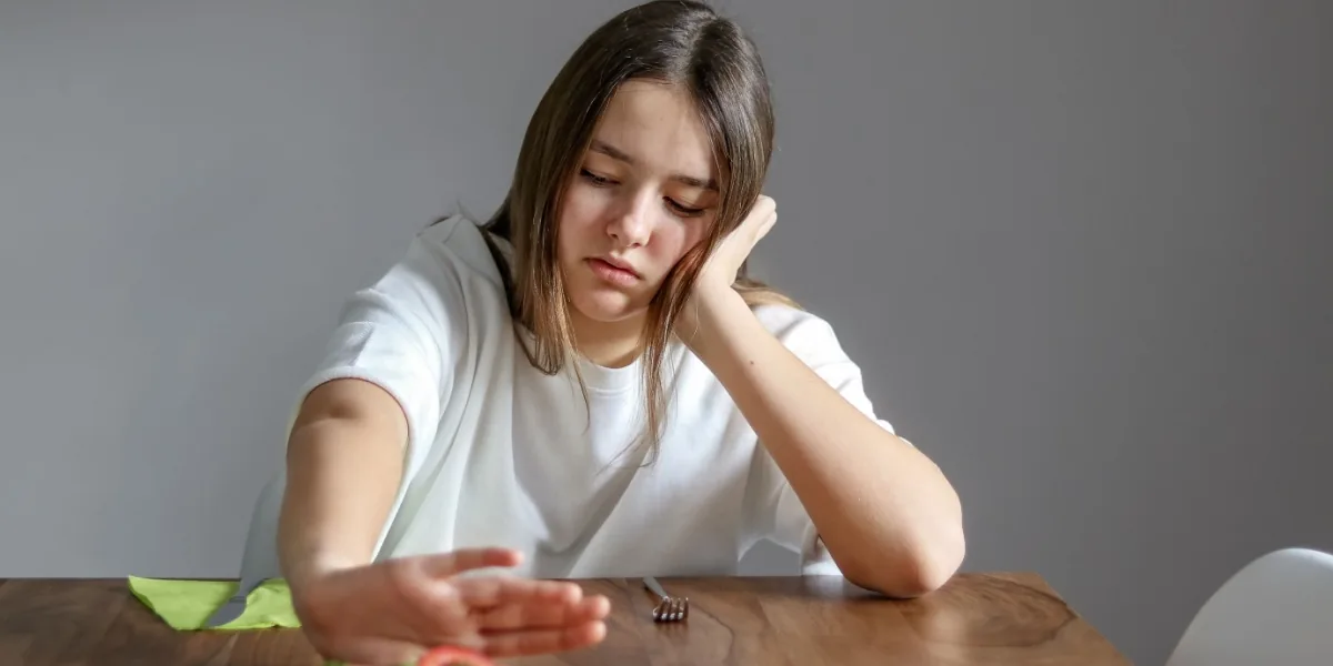 A woman sits thoughtfully at a table with a bowl in front of her.