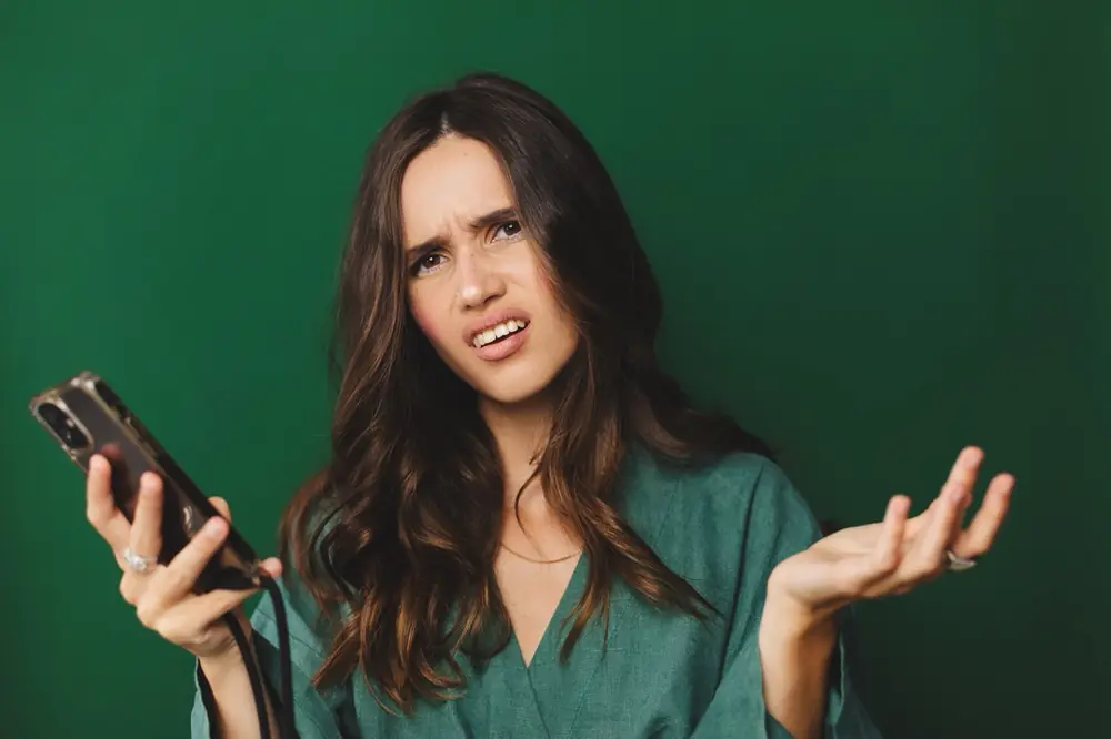 A woman holds a phone with a questioning expression.