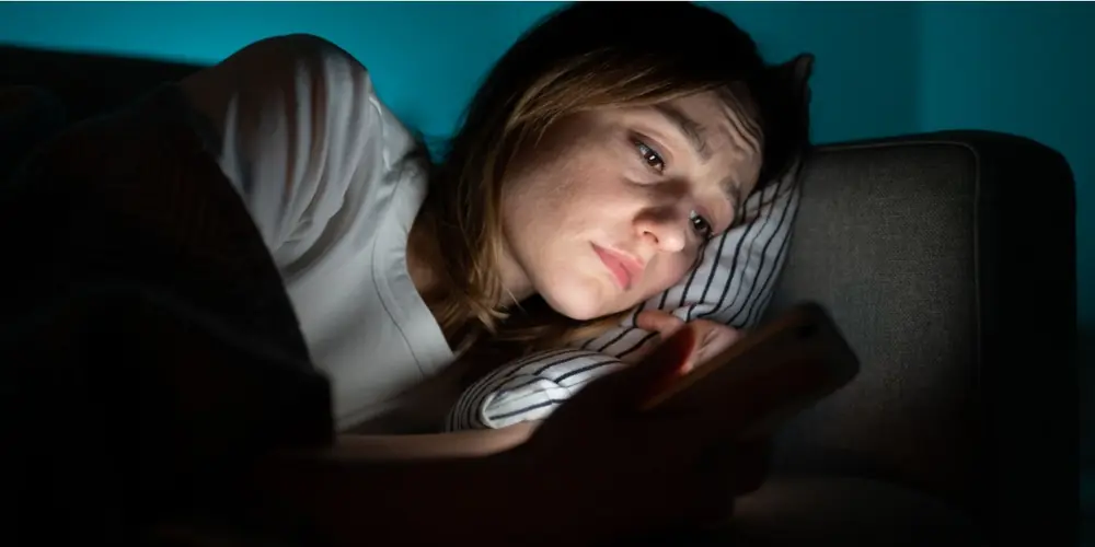 A person looks at an illuminated phone while lying down.