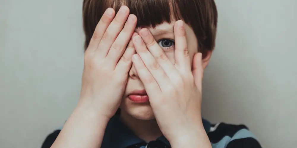 A child covers their eyes with both hands.