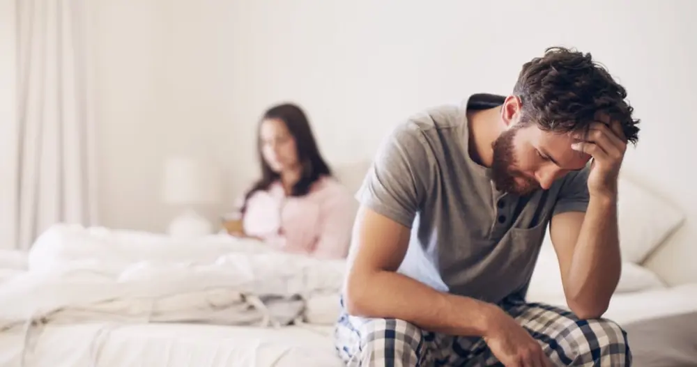 Two adults sit apart at the edge of a bed.
