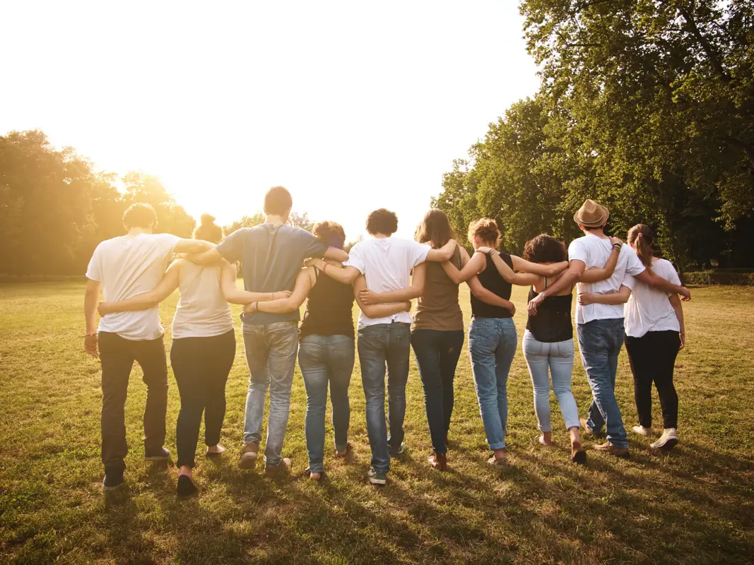 Friends stand arm in arm outdoors at sunset.