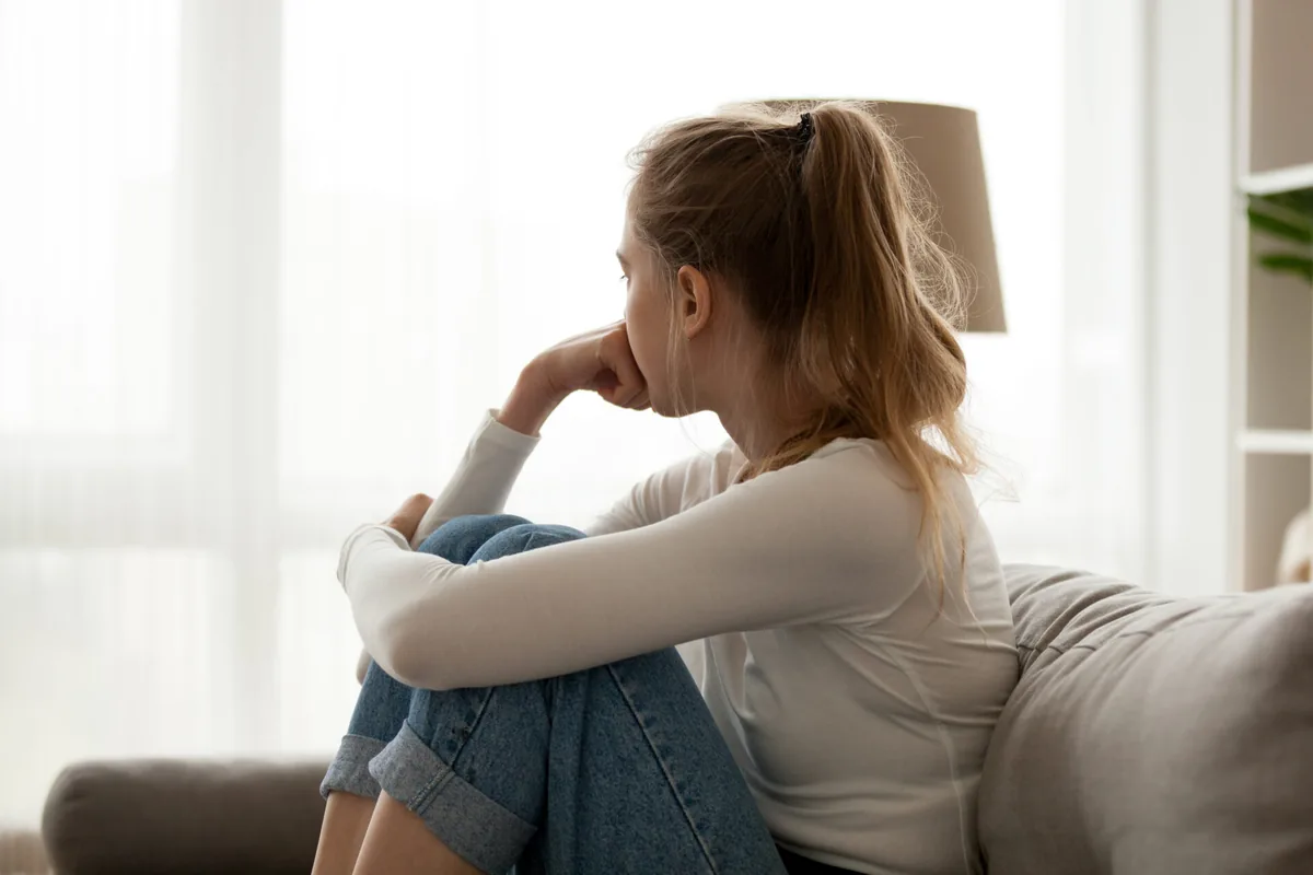 A woman rests her chin on her hand beside a window.