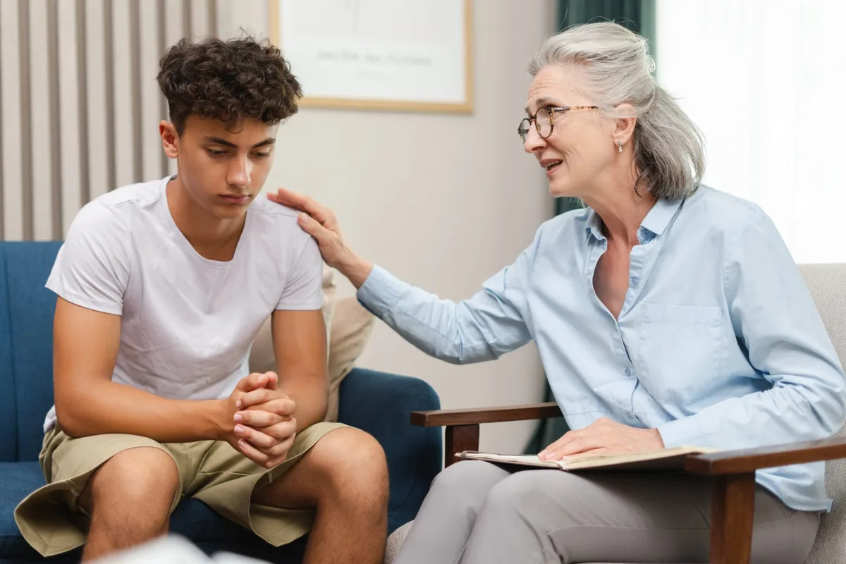 A young man talks with a counselor who rests a reassuring hand on his shoulder.
