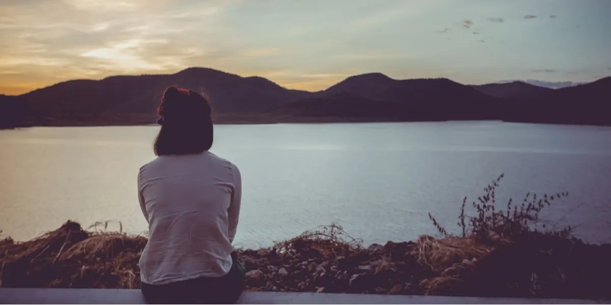 A person sits beside a lake and looks across the water.