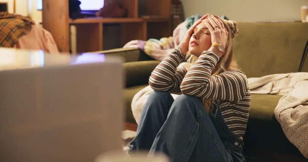 A woman sits with both hands near her face.