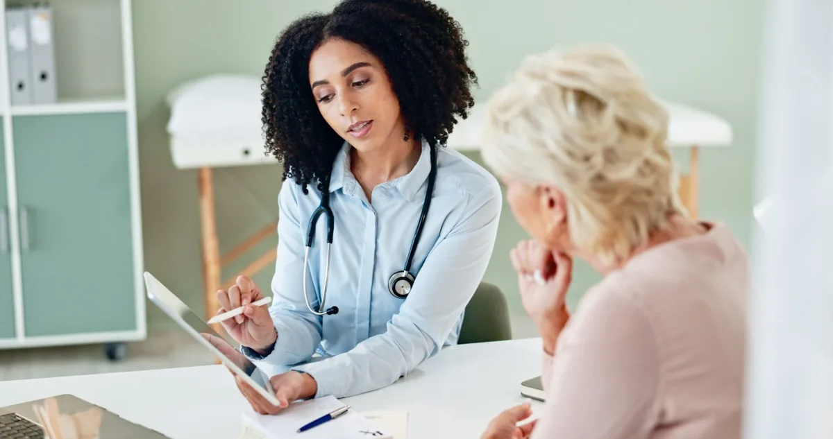 A healthcare professional writes notes while speaking with an older patient.
