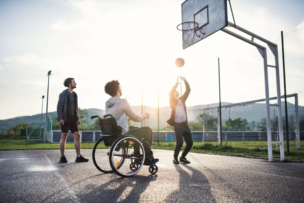 People play basketball together on an outdoor court, including a player using a wheelchair.