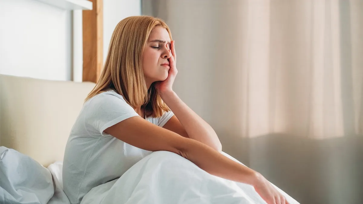 A woman sits quietly on a sofa with her arms resting on her knees.