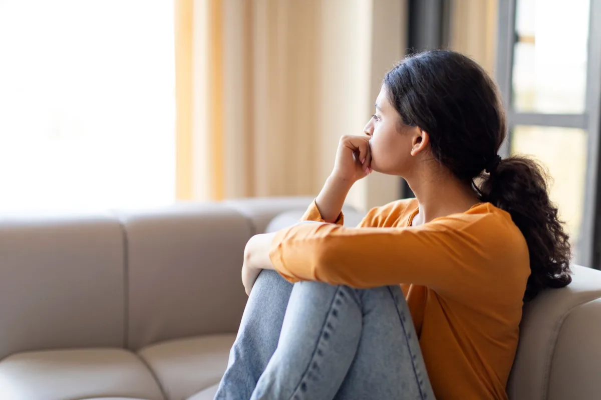 A woman sits quietly beside a sunlit window.