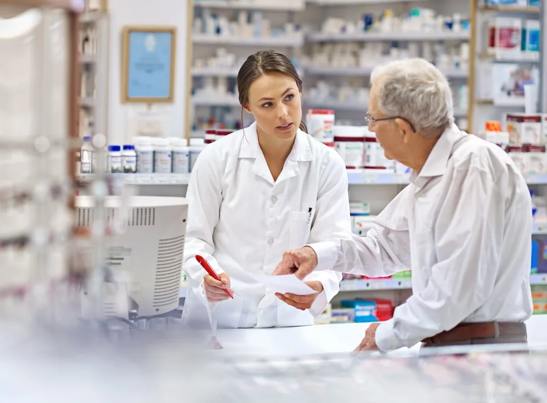 Healthcare professionals discuss information at a pharmacy counter.