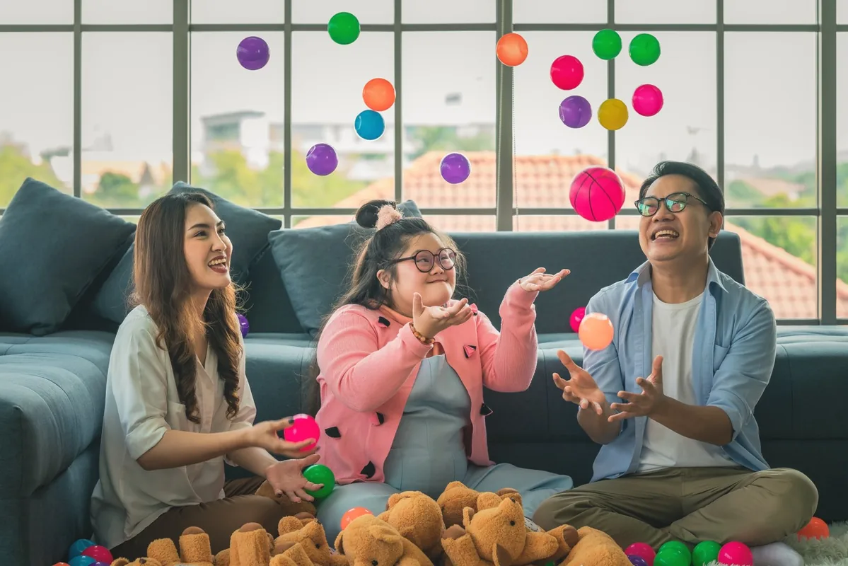 A child and adults play together with colorful objects in a bright room.